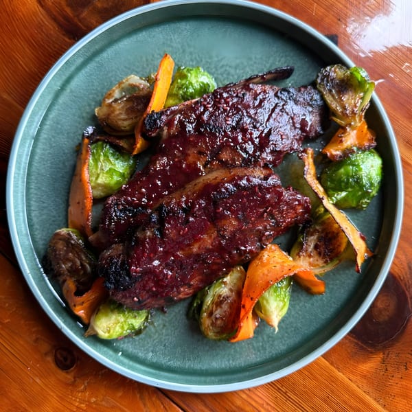 THE SPOT's Latin Fusion Cuisine features glazed ribs with roasted Brussels sprouts and carrots on a teal plate.