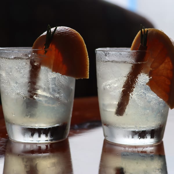 Two frosty cocktails garnished with grapefruit slices and rosemary sprigs on a reflective wooden surface.
