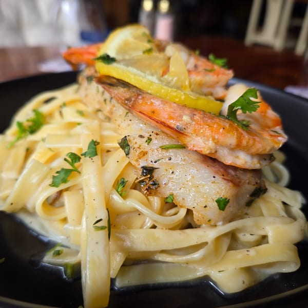 Fettuccine Alfredo pasta topped with grilled shrimp, fish, lemon slices, and fresh parsley.