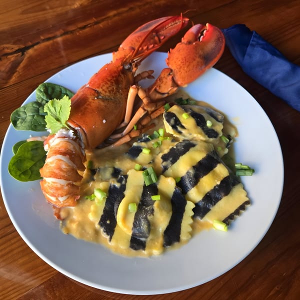 Whole cooked lobster and striped ravioli in a creamy sauce, garnished with greens and scallions.