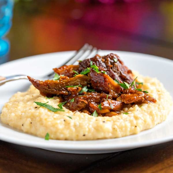 Savory brown meat and gravy over a bed of creamy yellow grits, garnished with fresh parsley.