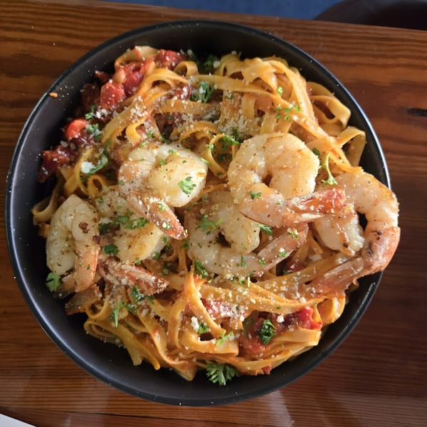 A black bowl of Latin Fusion Cuisine shrimp fettuccine pasta with tomato sauce, parmesan, and parsley.