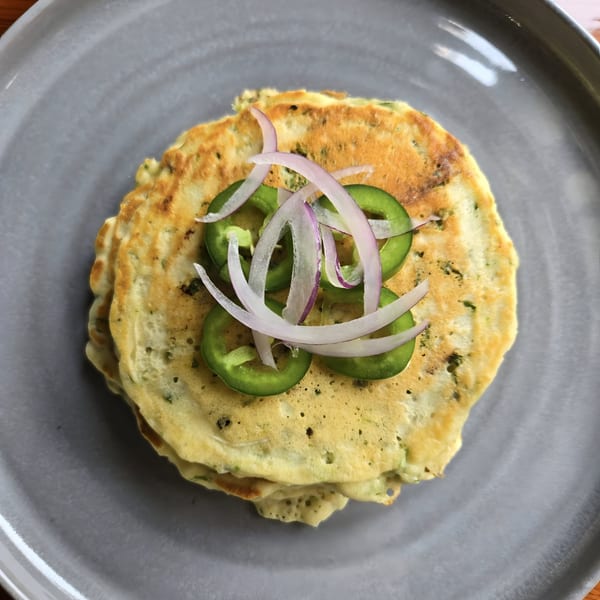 Savory Latin American pancakes topped with sliced green jalapeños and red onions on a gray plate.