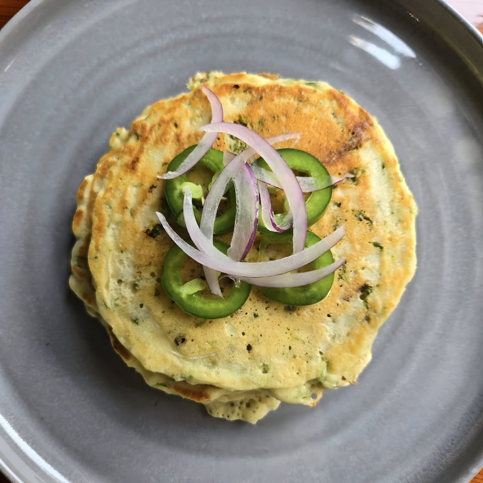 Savory Latin American pancakes topped with sliced green jalapeños and red onions on a gray plate.