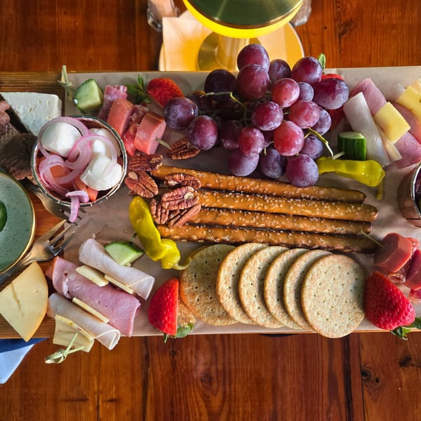 Overhead view of a charcuterie board with grapes, meats, cheeses, crackers, and pretzels.