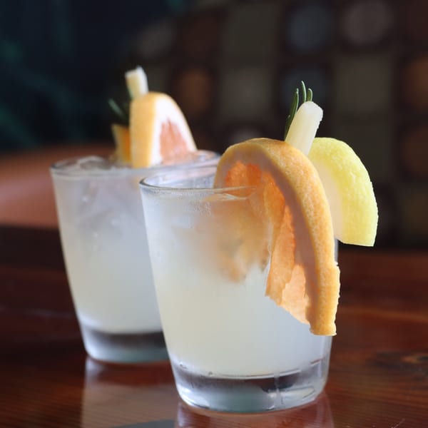 Two refreshing cocktails garnished with grapefruit, lemon, and rosemary on a wooden table.