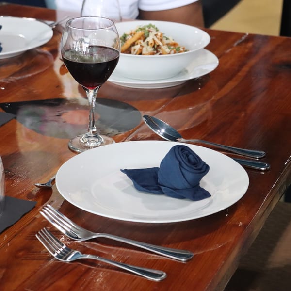 A dining table set with a white plate, blue napkin, silverware, wine glass, and pasta dish.