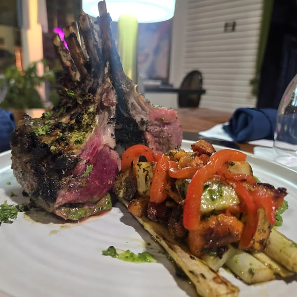 Rack of lamb with roasted vegetables and red peppers, served on a white plate at THE SPOT.