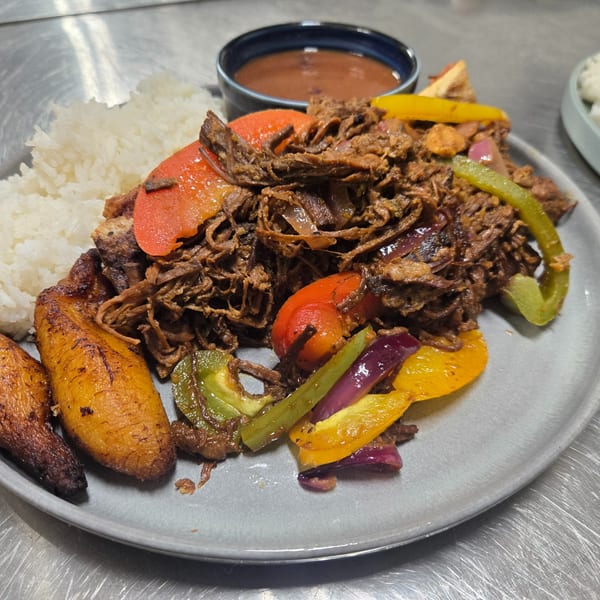 Shredded beef with colorful bell peppers, white rice, fried plantains, and a side of beans.